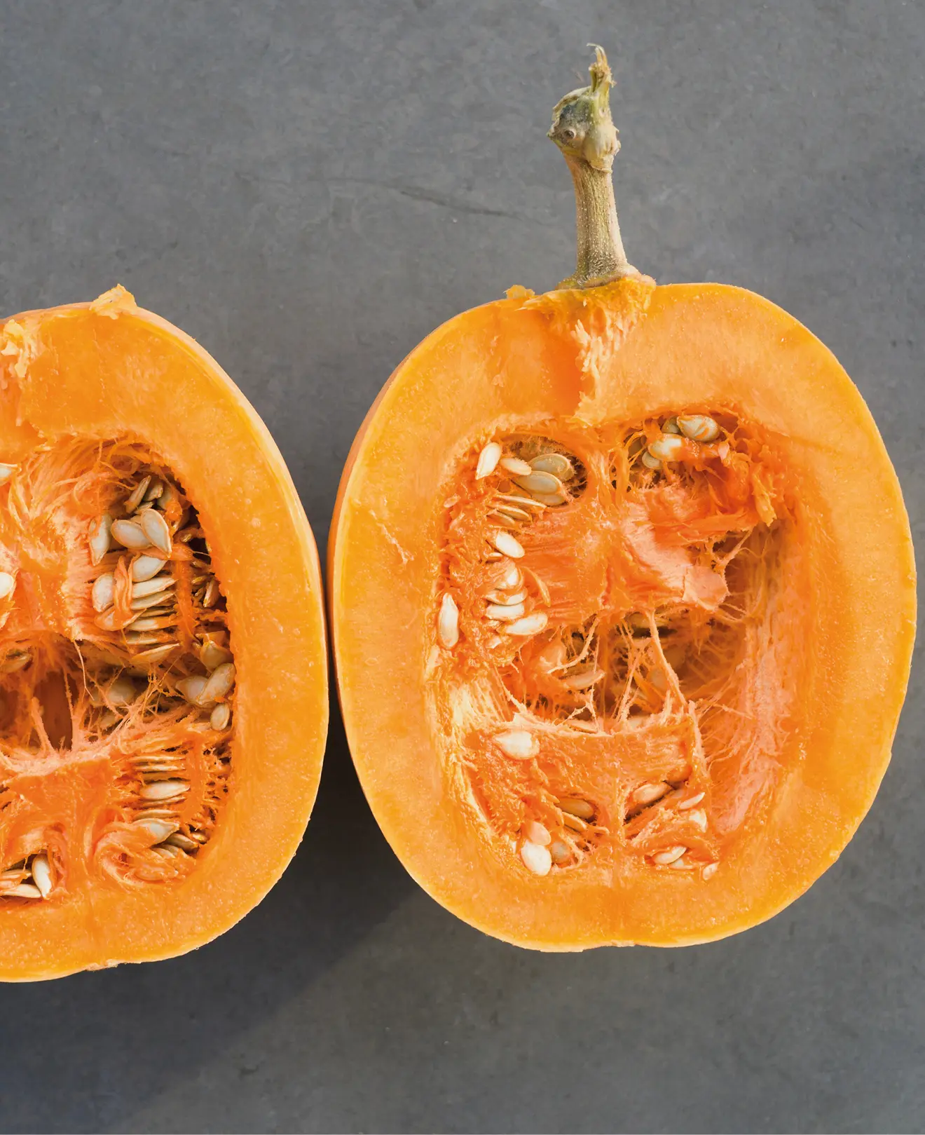 Aufgeschnittener Kürbis mit leuchtend orangefarbenem Fruchtfleisch und sichtbaren Kernen auf hellem Untergrund. Symbol für frisches Herbstgemüse, gesunde Ernährung und saisonales Kochen in der Küche.